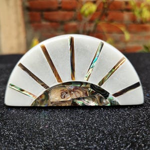 May include: A white, half-circle shaped, decorative object with a sunburst design made of iridescent mother of pearl. The object is made of white marble and has a smooth, polished surface.