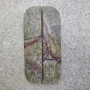 May include: Two rectangular coasters with rounded tops, featuring a split design. The coasters display a green, brown, and red marbled pattern. They are set against a textured, grey background.