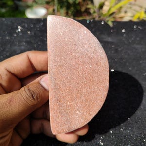 May include: A semi-circular, reddish-brown stone with a textured surface. The stone is held in a hand against a dark, glittery background. The object appears to be a decorative or natural item, possibly for home decor or crafting.