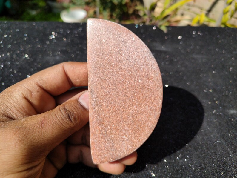 May include: A semi-circular, reddish-brown stone with a textured surface. The stone is held in a hand against a dark, glittery background. The object appears to be a decorative or natural item, possibly for home decor or crafting.