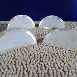 May include: Set of four white mother of pearl napkin rings with a yellow iridescent trim.