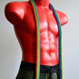 May include: A rainbow lei made of braided ribbon with long tails. The lei is worn by a mannequin wearing green and black patterned shorts.