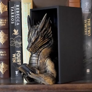 May include: A shelf displays books and dragon bookends. The books include titles like "The Hobbit" and "The Fellowship of the Ring." The dragon bookends are bronze-colored and add a fantasy theme to the bookshelf.