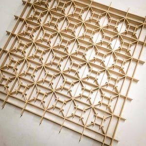 May include: A wooden lattice panel with a geometric pattern. The panel is made of thin strips of wood that are arranged in a grid pattern. The panel is light brown in color and has a natural wood finish.