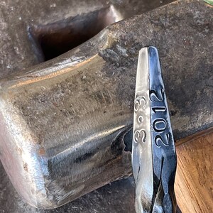 May include: Close-up of a metal hammer head with the numbers "3-9-3" and "2012" engraved on the side.