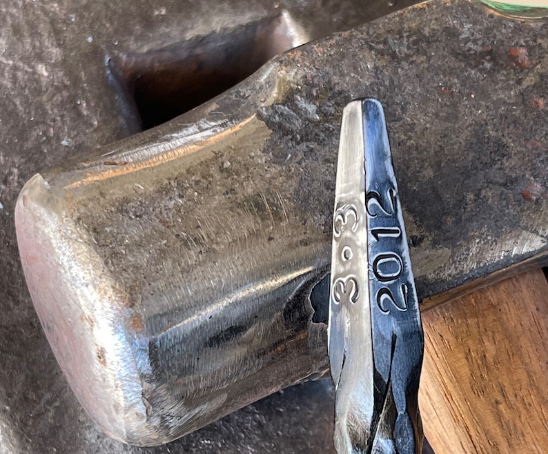May include: Close-up of a metal hammer head with the numbers "3-9-3" and "2012" engraved on the side.