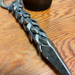 May include: A silver bottle opener with a unique, textured, and pointed design. The opener has a loop at the top for opening bottles.