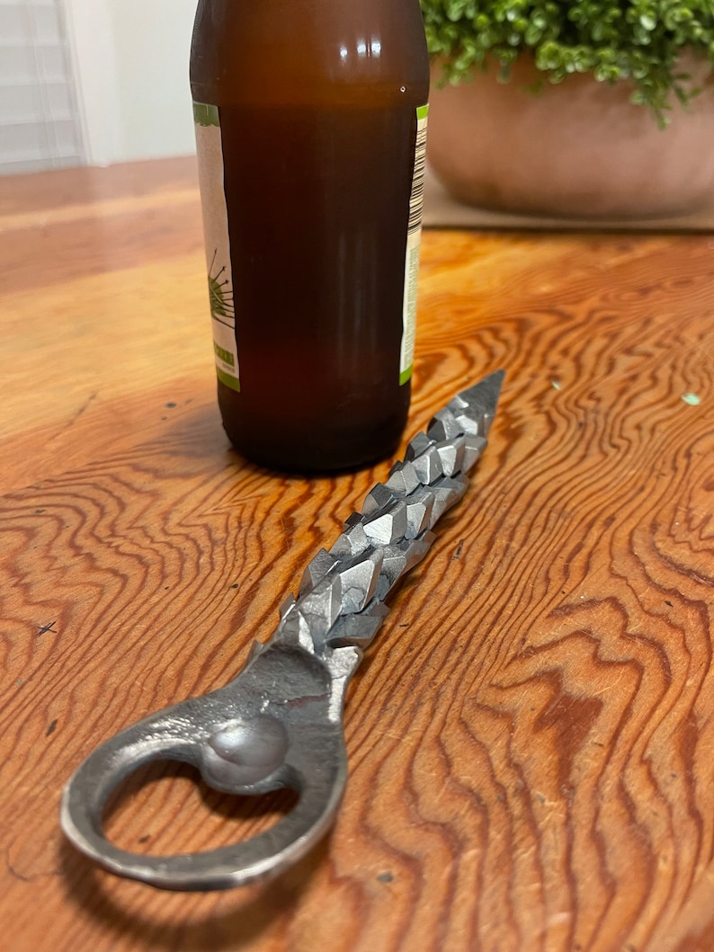 May include: A silver bottle opener with a textured, jagged handle. The opener is lying on a wooden surface.