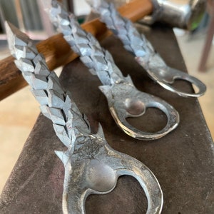 May include: Three silver bottle openers with a textured, twisted design. The bottle openers are made of metal and have a loop at the top for hanging.