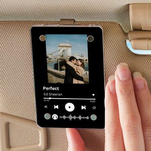 May include: A black phone case with a clear window displaying a photo of a couple in front of a bridge. The phone case has a music player interface with the song "Perfect" by Ed Sheeran playing.