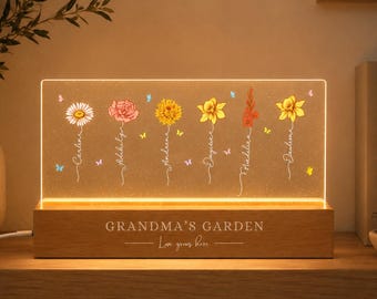 May include: A rectangular acrylic night light with a wooden base featuring the engraved text "GRANDMA'S GARDEN" and "Love grows here." The acrylic panel displays six colorful illustrated flowers with names written on their stems and small butterflies.