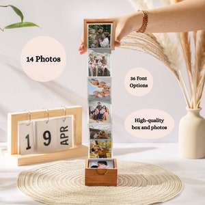 Könnte beinhalten: Eine Holzkiste mit einem herausziehbaren Fotostreifen mit 14 Fotos einer Familie. Die Kiste steht auf einem Tisch mit einem Kalender, auf dem "19 APR" steht.