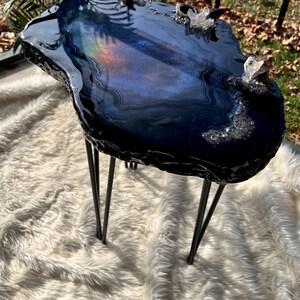 May include: A side table with a dark blue and black resin top featuring an irregular, geode-inspired shape. The surface has a glossy finish with embedded clear quartz crystals and thin black metal hairpin legs supporting the structure.