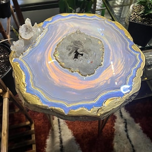 May include: A round side table featuring a faux agate slice top with concentric layers of light blue, white, and iridescent orange. The center and one edge are embedded with clear quartz crystals. The table has a thick, textured gold painted edge.