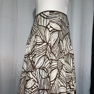 May include: A-line skirt with a white background and a brown leaf pattern. The skirt has a brown border at the hem and waist. The skirt is displayed on a mannequin.
