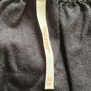 Może przedstawiać: Czarna metka odzieżowa Free People z białym tekstem, kt&oacute;ry brzmi "Made in India / Fabriqu&eacute; en Inde" i "XS TP".