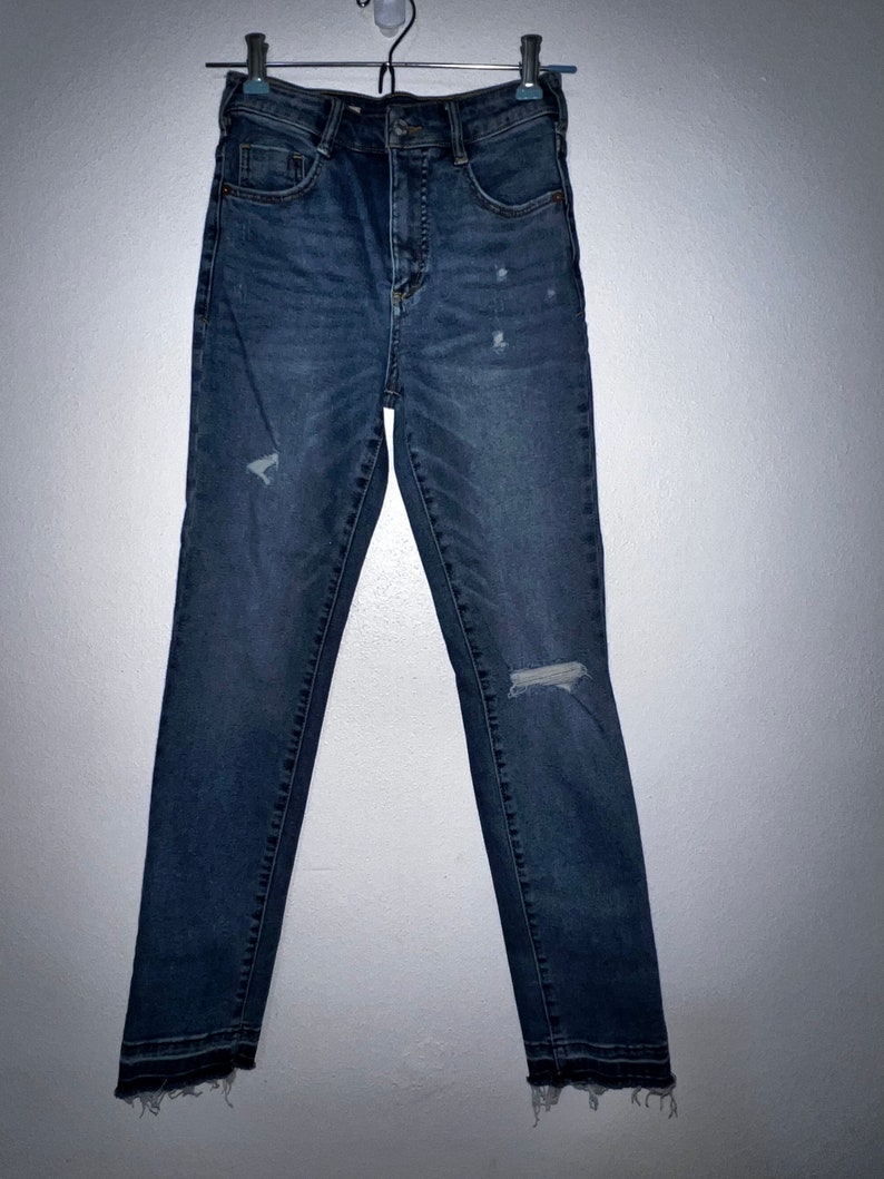 May include: A pair of dark blue denim jeans with distressed details and a frayed hem.