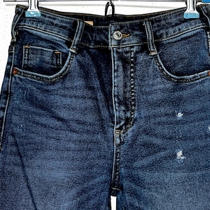 May include: A pair of dark blue denim jeans with a light wash and a distressed look. The jeans have a high waist and a straight leg.