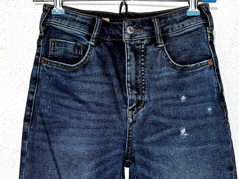 May include: A pair of dark blue denim jeans with a light wash and a distressed look. The jeans have a high waist and a straight leg.
