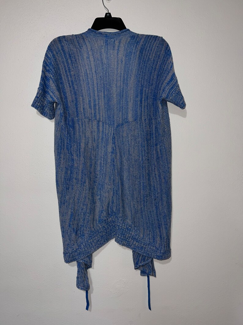 Puede incluir: Un c&aacute;rdigan de punto azul y gris con mangas cortas y un lazo en la parte inferior.