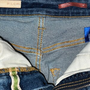 May include: Close-up of the inside of a pair of blue denim jeans. The jeans have a high rise and a cigarette fit. The label reads "High Rise Cigarette".