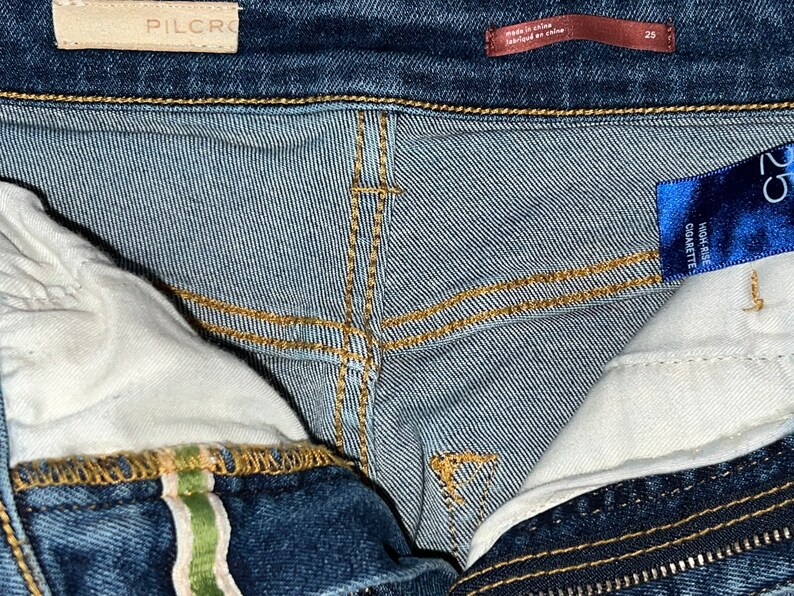 May include: Close-up of the inside of a pair of blue denim jeans. The jeans have a high rise and a cigarette fit. The label reads "High Rise Cigarette".