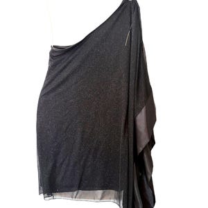 May include: A black one-shoulder dress featuring a shimmering, glittery fabric finish. The garment has a draped, asymmetrical silhouette with a smooth, solid black fabric panel along the side, creating a layered effect that falls to the hemline.