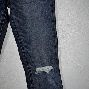 May include: Dark blue denim jeans with distressed details, featuring a small hole on the knee.