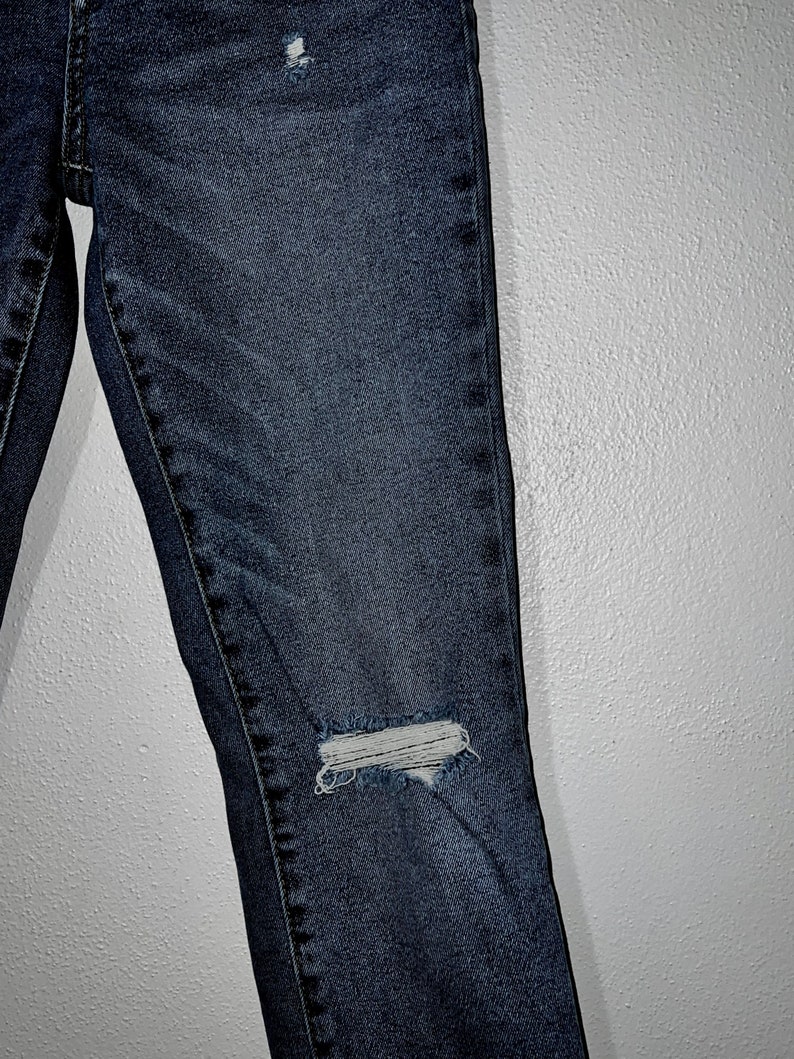 May include: Dark blue denim jeans with distressed details, featuring a small hole on the knee.