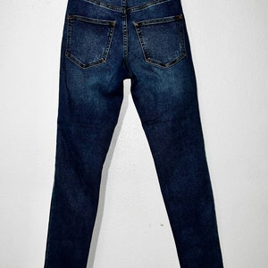 May include: Dark blue denim jeans with a frayed hem. The jeans have a high waist and a slim fit.