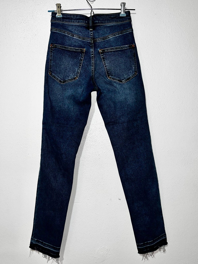 May include: Dark blue denim jeans with a frayed hem. The jeans have a high waist and a slim fit.