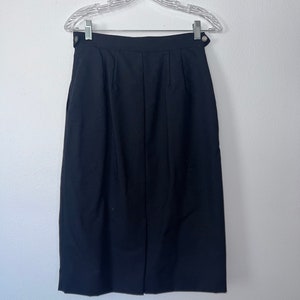 May include: A black knee-length skirt with a straight silhouette and a simple design. The skirt has a button closure at the front and two pleats on each side.