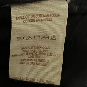 Może przedstawiać: Beige etykieta pielęgnacyjna z tkaniny z instrukcjami prania, suszenia i prasowania. Etykieta zawiera napis "100% Bawełna Coton Algod&oacute;n Cotone Baumwolle", "Prać w pralce w zimnej wodzie z podobnymi kolorami", "Używać tylko wybielacza bez chloru", "Suszyć na linie", "Prasować w niskiej temperaturze w razie potrzeby", "Można czyścić chemicznie".