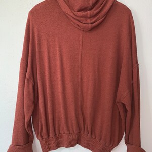 Op de afbeelding: Een roestkleurig hooded sweatshirt met een elastische tailleband en gemanchetten.