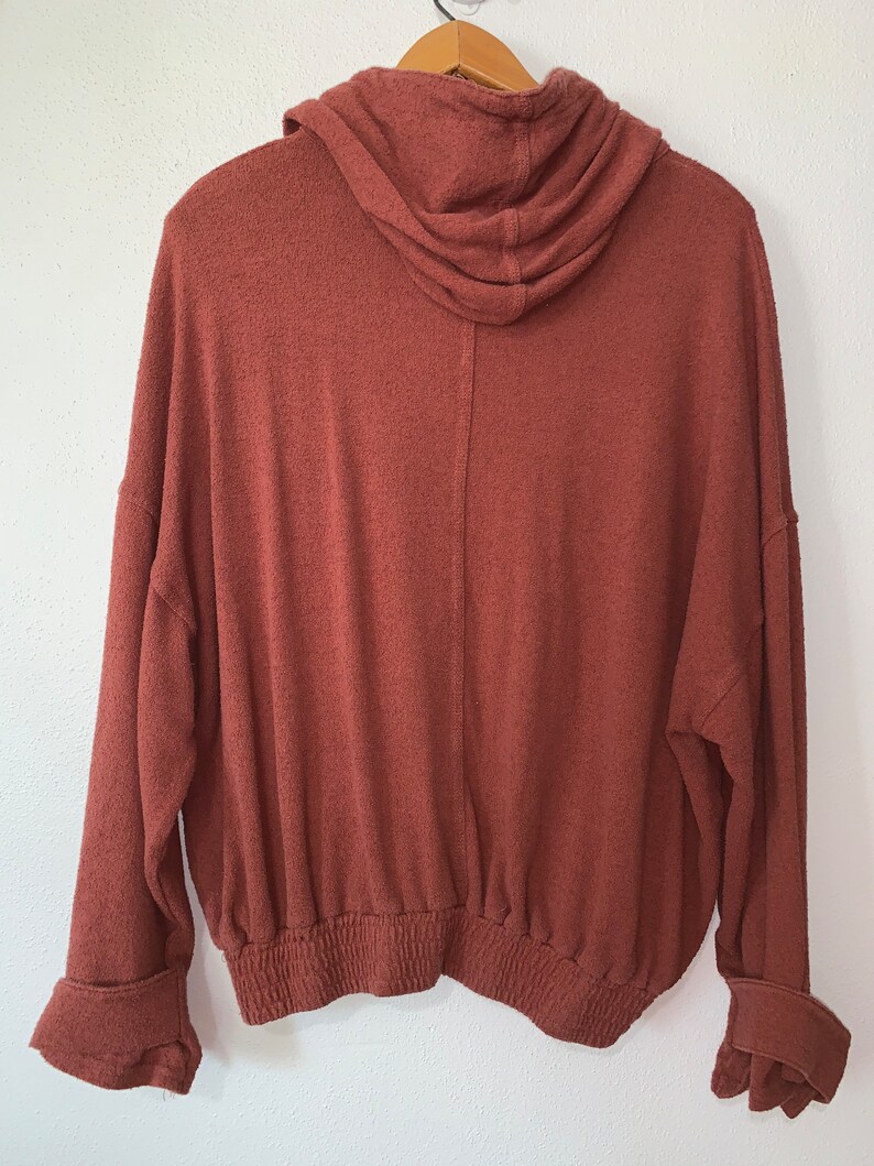 Op de afbeelding: Een roestkleurig hooded sweatshirt met een elastische tailleband en gemanchetten.