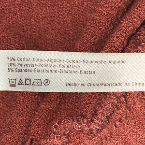 Op de afbeelding: Een wit stoffen label met bruine tekst en wasinstructies. Het label vermeldt: 75% Katoen-Coton-Algod&oacute;n-Cotone-Baumwolle-Algod&atilde;o 20% Polyester-Poliester-Poliestere 5% Spandex-Elasthanne-Elastano-Elastan Hecho en China/Fabricado na China. Het label bevat ook een wasinstructiesymbool.