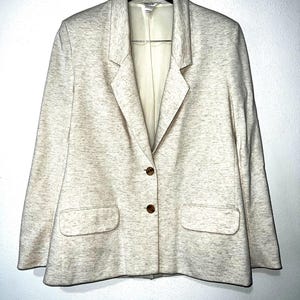 May include: A cream-colored blazer with a subtle speckled pattern. It has a notched collar, two button closures, and two front pockets.