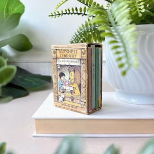 May include: A miniature boxed set titled Nutshell Library by Maurice Sendak, featuring a beige slipcase with an illustration of a child and a lion. The set contains four small books with spines in shades of pink, green, and yellow, published by Harper & Row.