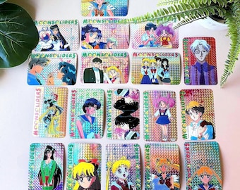 Puede incluir: Colección de tarjetas coleccionables rectangulares con personajes de anime. Las tarjetas tienen un acabado holográfico iridiscente y el texto "MOONSOLIDERS" está impreso en cada una. Los personajes se representan en varias poses y atuendos, con colores vibrantes.
