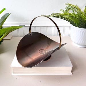 May include: A brown metal basket with a gold handle. The basket is sitting on a white book.