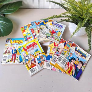 以下が含まれることがあります： ヴィンテージの「Laugh Digest Magazine」コミック本のコレクション。表紙には、漫画のキャラクターのカラフルなイラストが描かれています。雑誌は明るい色の表面に配置され、背景にはシダがあります。「Laugh Digest Magazine」のテキストが表紙に表示されています。