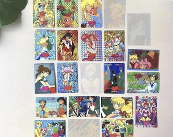 Puede incluir: Una colección de veinticuatro tarjetas coleccionables rectangulares de Sailor Moon dispuestas en una cuadrícula. Las tarjetas muestran varios personajes de anime con atuendos coloridos, patrones holográficos y poses de acción, algunas de ellas semitransparentes.
