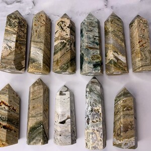 May include: A collection of 12 green, brown, and white banded agate crystal points. The points are all different sizes and shapes, but they are all polished and have a smooth, shiny finish.