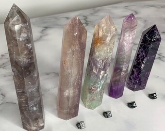 May include: Five different fluorite crystal points, each with a unique color and pattern. The crystals are arranged in a row from left to right, with numbers 1 through 5 placed below each crystal.