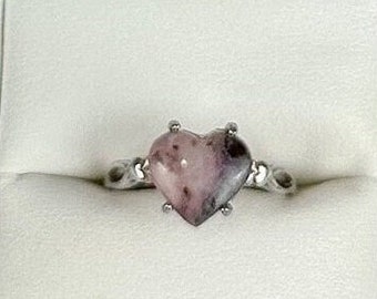 May include: A heart-shaped ring with a pink and white gemstone set in a silver band. The ring is displayed in a black ring box.