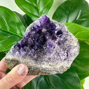May include: A large amethyst crystal cluster with a natural, rough exterior and a deep purple color. The crystal is a natural formation with a variety of sizes and shapes of amethyst crystals.