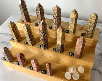 May include: A set of 14 colorful, multi-colored, polished, pointed, crystal, gemstone, or mineral, wands or towers on a wooden display stand. The stand has three tiers and is made of bamboo. There are also four clear quartz stones on the bottom tier of the stand.