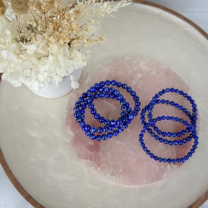 May include: Two sets of blue lapis lazuli beaded bracelets on a pink rose quartz background.