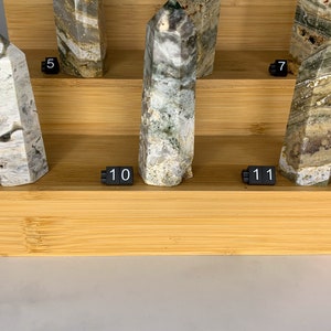 May include: A display of nine green and white crystal points on a wooden shelf. The crystals are numbered 5, 7, 8, 9, 10, and 11.