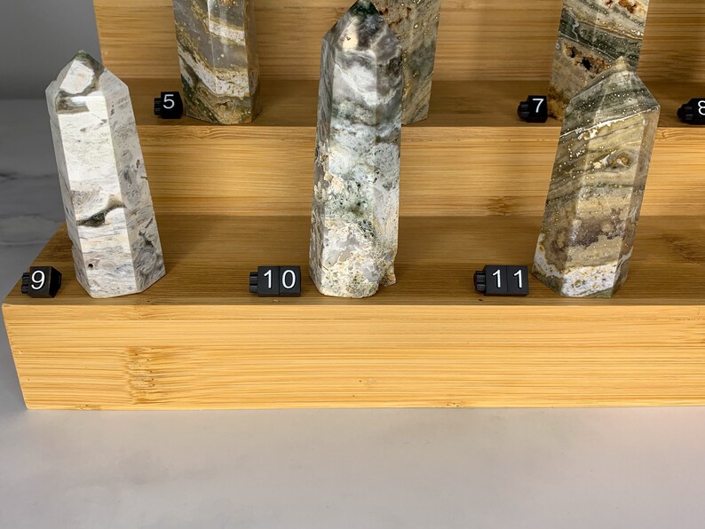 May include: A display of nine green and white crystal points on a wooden shelf. The crystals are numbered 5, 7, 8, 9, 10, and 11.